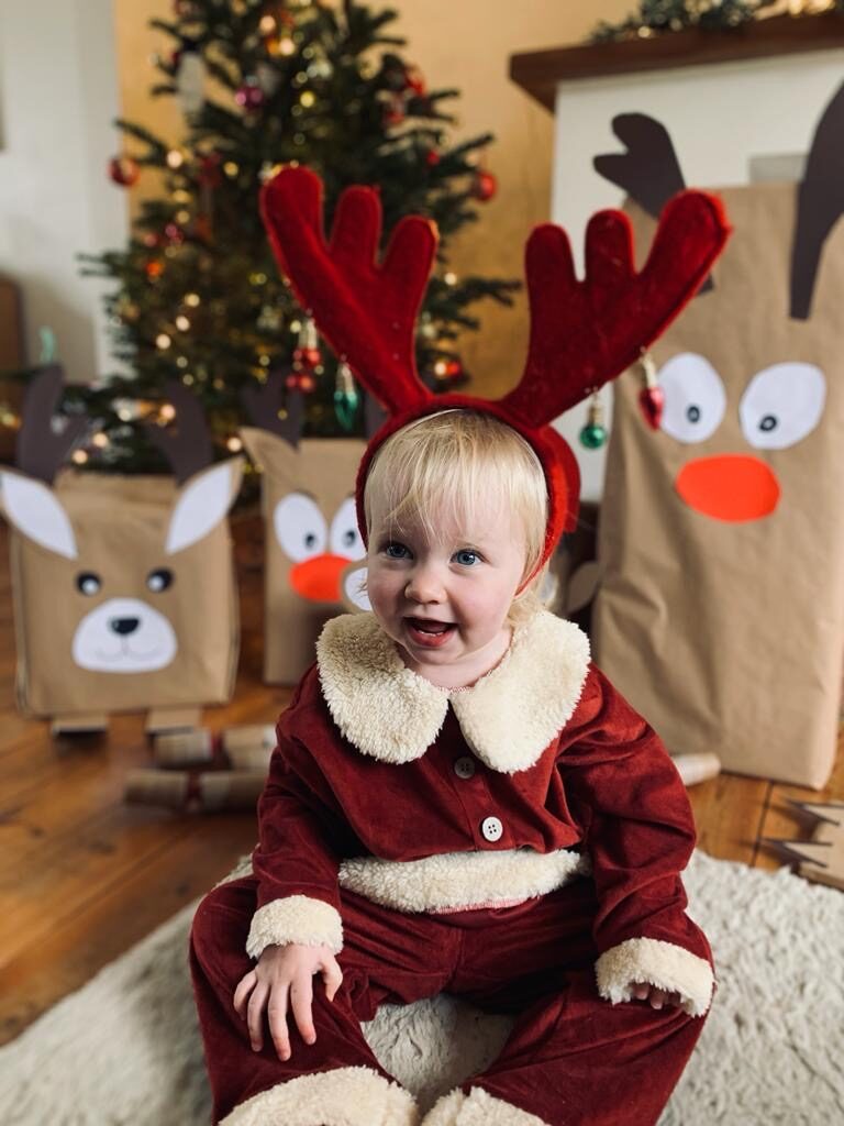 Baby sat under the Christmas tree dressed in a Christmas outfit in front of presents